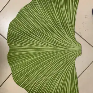 Groene badmat in de vorm van een blad op lichte tegels