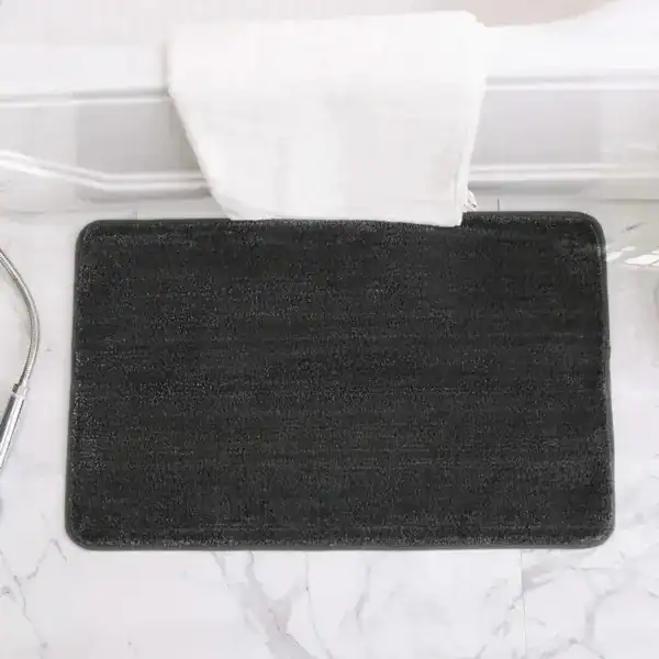 Zwarte badmat met antislip onderkant voor badkamer, op marmeren vloer voorzien van een witte handdoek.
