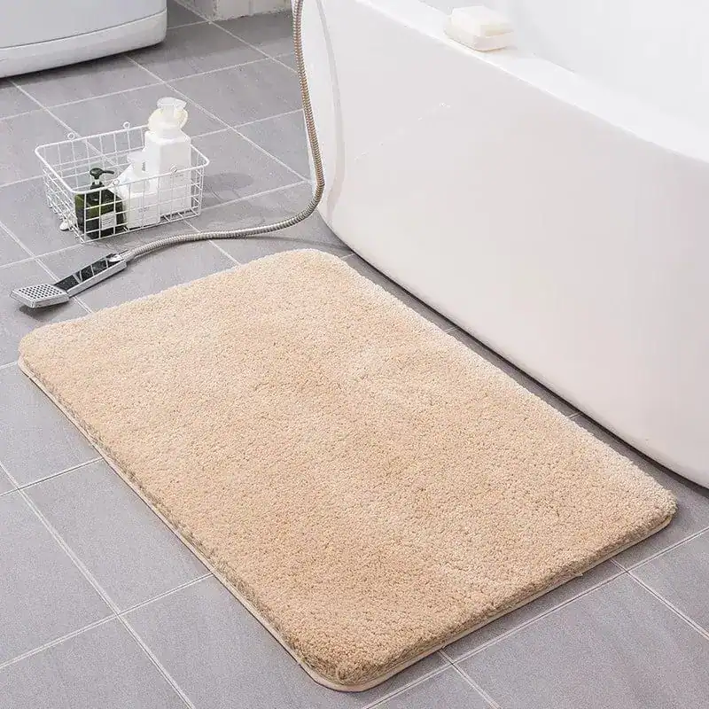 Fluffy badmat in beige kleur, geplaatst voor de badkuip op grijze tegels.