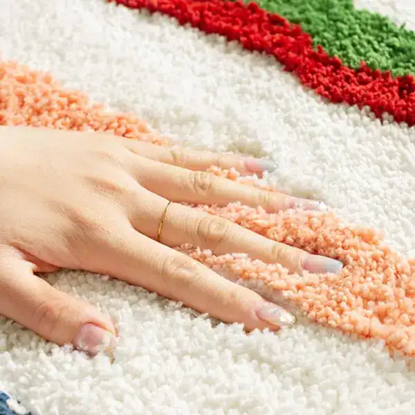 Kleurrijke badmat met witte, roze, rode en groene strepen, hand op de mat.