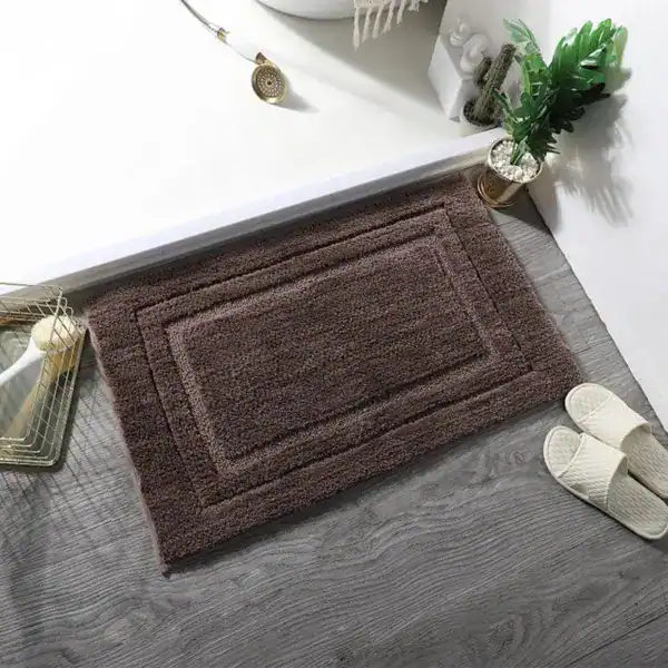 Donkergrijze badmat met dubbele rand, geplaatst voor een witte badkuip in een moderne badkamer.