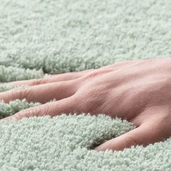 Zachte badkamermat in mintgroen, met hand op de textuur.